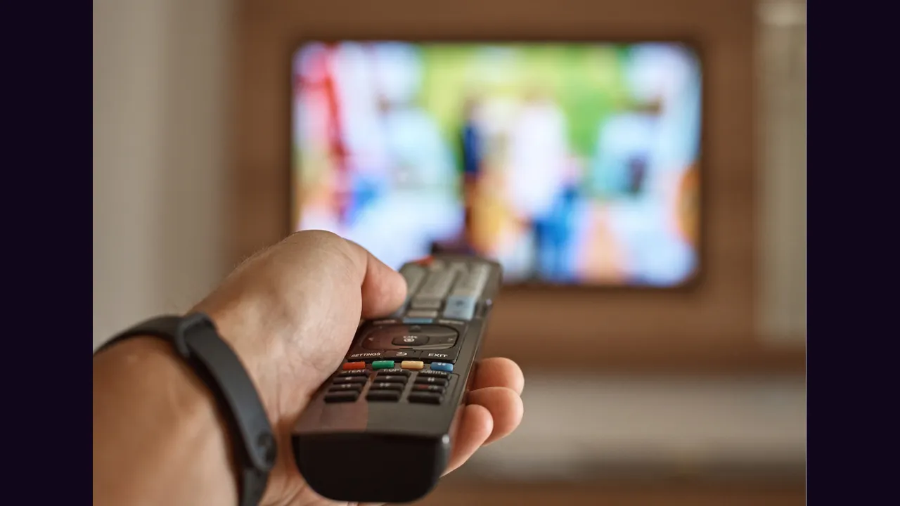 A hand holding a television remote control aimed at a television